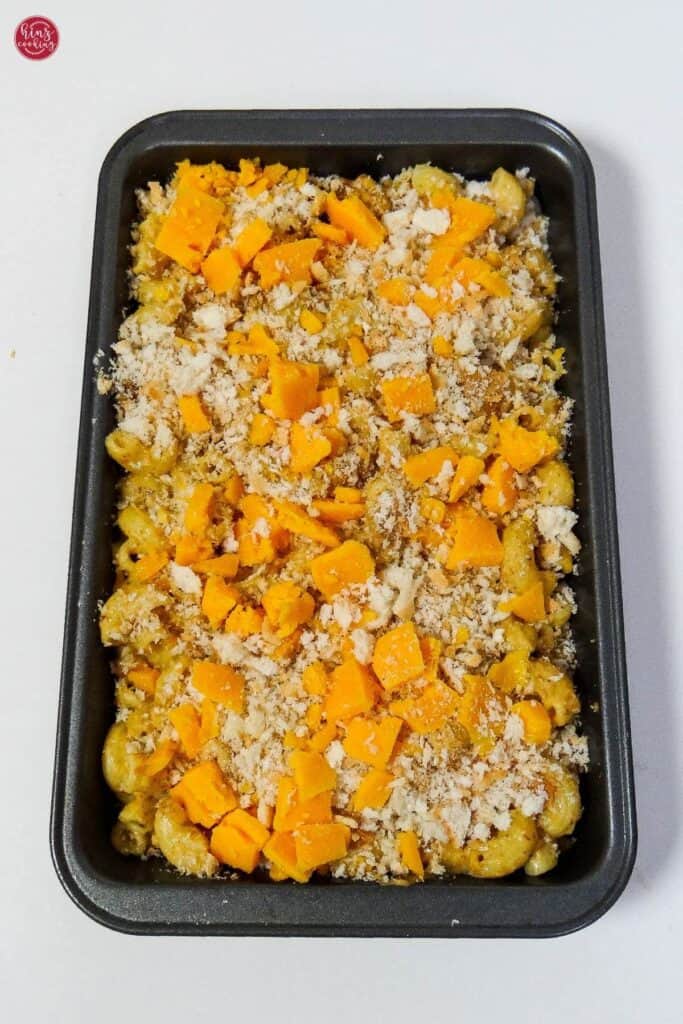 Cajun chicken mac and cheese topped with panko bread crumbs and cheddar cheese. Set in black baking dish with white background.