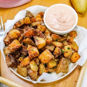 Golden-brown, extra crispy air fryer potatoes served on a white platter with a side of house dipping sauce.